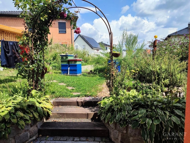 Kräuterspirale und Rosenbogen im Sommer